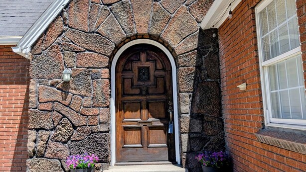 Fachada de pedra com porta de madeira, degraus de tijolo e uma janela.