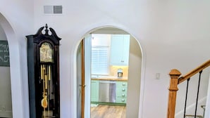 Um corredor com piso de madeira, um relógio e uma escada que dá acesso a uma cozinha.