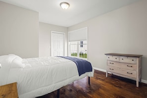 A bedroom with a bed, dresser, and a door leading to another room.