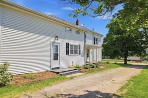 A two-story white house with a front porch, a satellite dish, and a tree in the background.