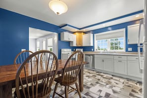 A modern kitchen with blue walls, white cabinets, a wooden dining table, and a patterned floor.