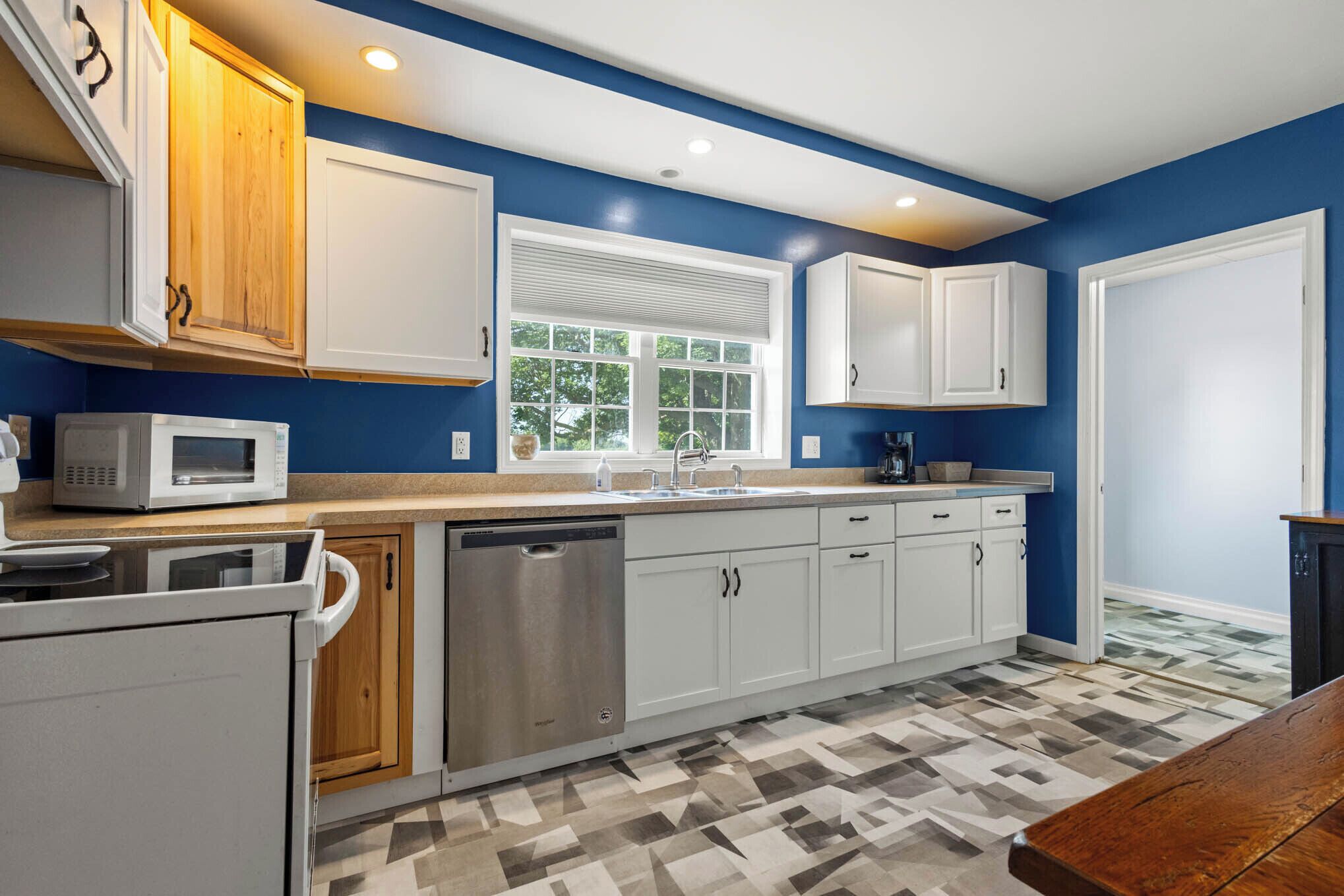 A kitchen with white cabinets, a microwave, a dishwasher, and a window with blinds.