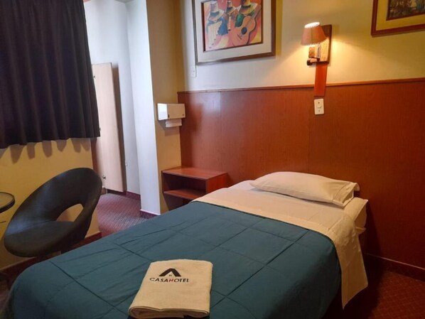Een hotelkamer met een bed, een stoel, een nachtkastje, een lamp en een schilderij aan de muur.