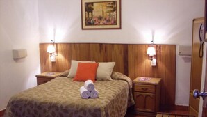 A room with two beds, wooden headboard, bedside lamps, a wooden bench, and a painting on the wall. - GrupoCasahotel Accommodation 5 minutes away from Jockey Plaza, Rambla, Museo de Nación (Ate)