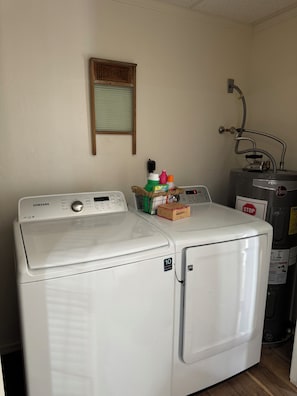 Une buanderie Ă©quipĂ©e dâun lave-linge et dâun sĂšche-linge Samsung, dâun chauffe-eau et dâun panneau de signalisation « stop » fixĂ© au mur.