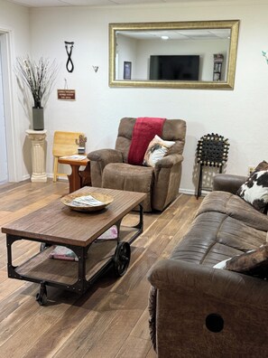 Una sala de estar con sofá, mesa de centro, sillón, espejo y un adorno en la pared.