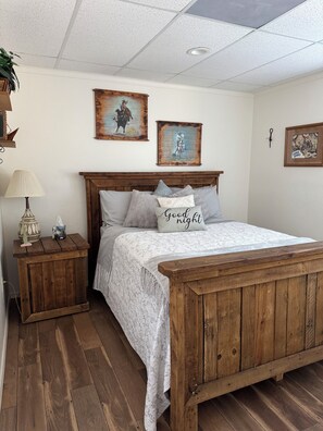 Un dormitorio con una cama de madera, una mesita de noche con una lámpara y dos cuadros colgados en la pared.