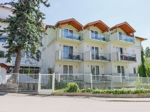 Ein mehrstöckiges Hotel mit Balkonen, einem weißen Zaun und einem Baum davor.