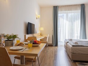 Une chambre d’hôtel comprenant un lit, un bureau avec une chaise, une télévision, une fenêtre avec des rideaux et une plante.