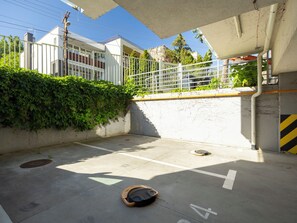 Ein Parkplatz mit Betonbefestigung, gekennzeichneten Stellplätzen, einem Abdeckungsrost und einem Metallzaun mit Bepflanzung.