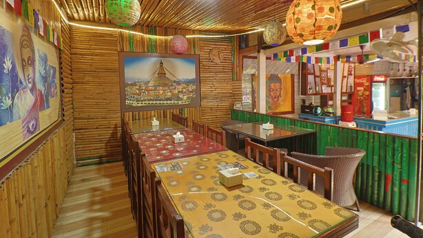 A restaurant with wooden walls, a long table with a patterned tablecloth, and various decorations including a Buddha painting and a globe. - Hotel Lekali Homes  (Kathmandu)