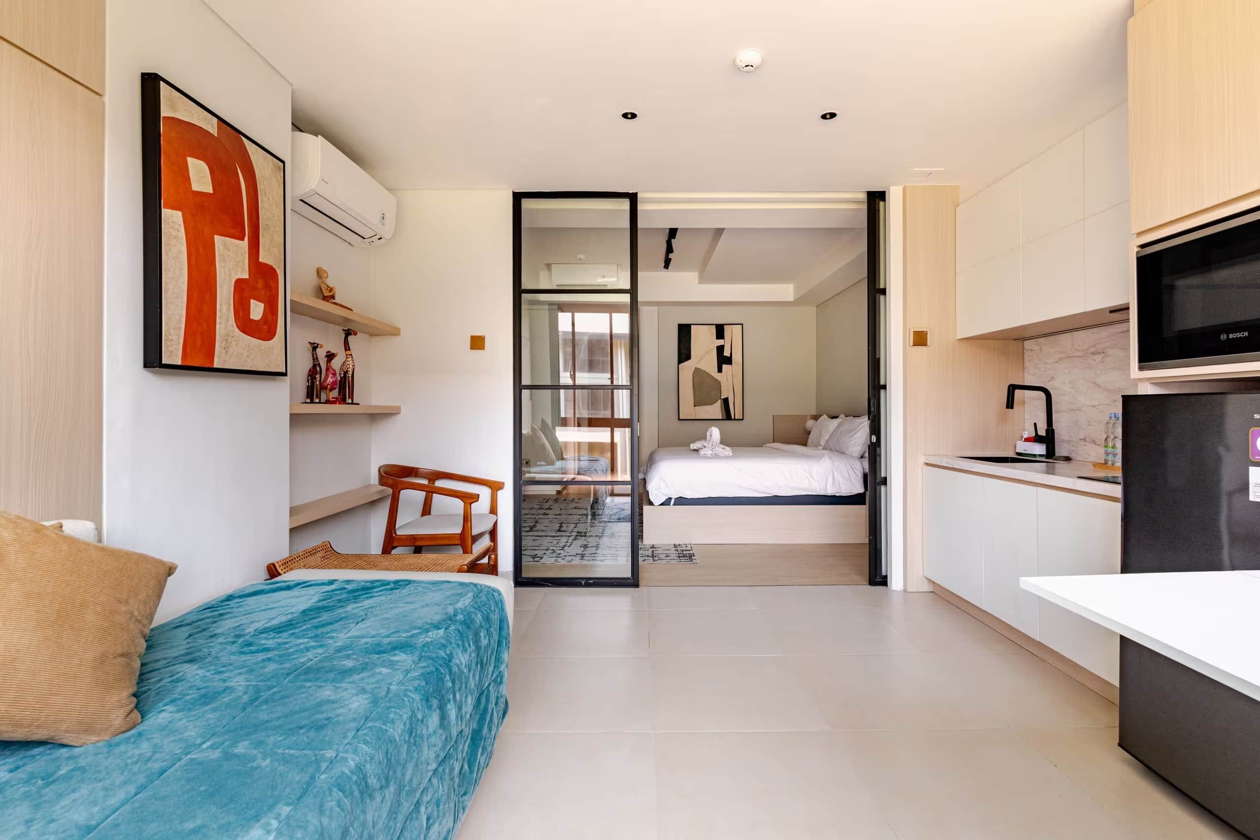 A modern bedroom with a bed, a chair, a desk, and a kitchenette.
