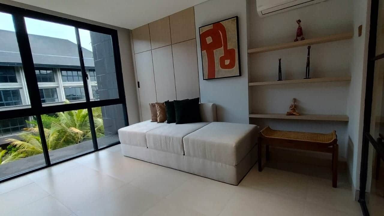 Una habitación moderna con un ventanal grande, un sofá, un banco y estanterías con objetos decorativos.