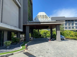 A hotel entrance with a covered walkway, a sign reading 'Deluxe,' and a parking area with a car.
