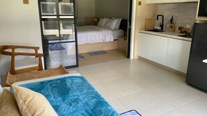 Ein gemütlicher Raum mit Bett, Stuhl, Küchenzeile und einer Schiebetür zu einem weiteren Raum.