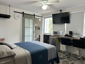 Ein Schlafzimmer mit Bett, Schreibtisch, Fernseher, Mikrowelle und Kaffeemaschine.