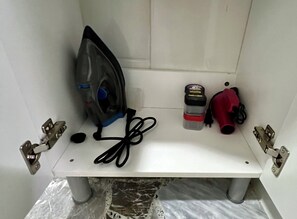 Ein kleines Badezimmer mit einer weißen Ablage, einem Bügeleisen, einem roten Fön und einer Handdesinfektionsmittel-Flasche.