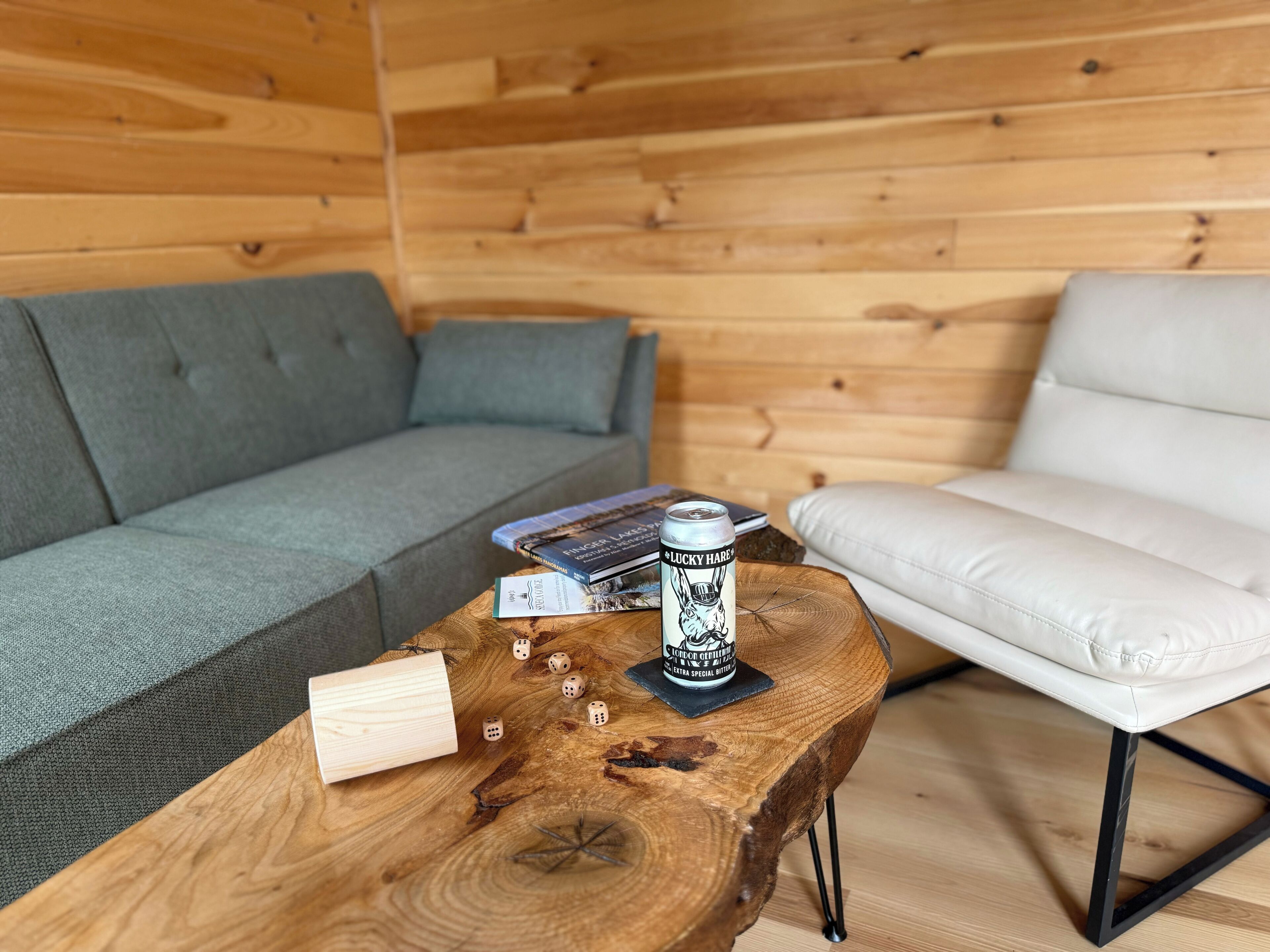 Een knus interieur met een grijze bank, een witte stoel, een houten bijzettafeltje met boeken en dobbelstenen, en een blikje bier.