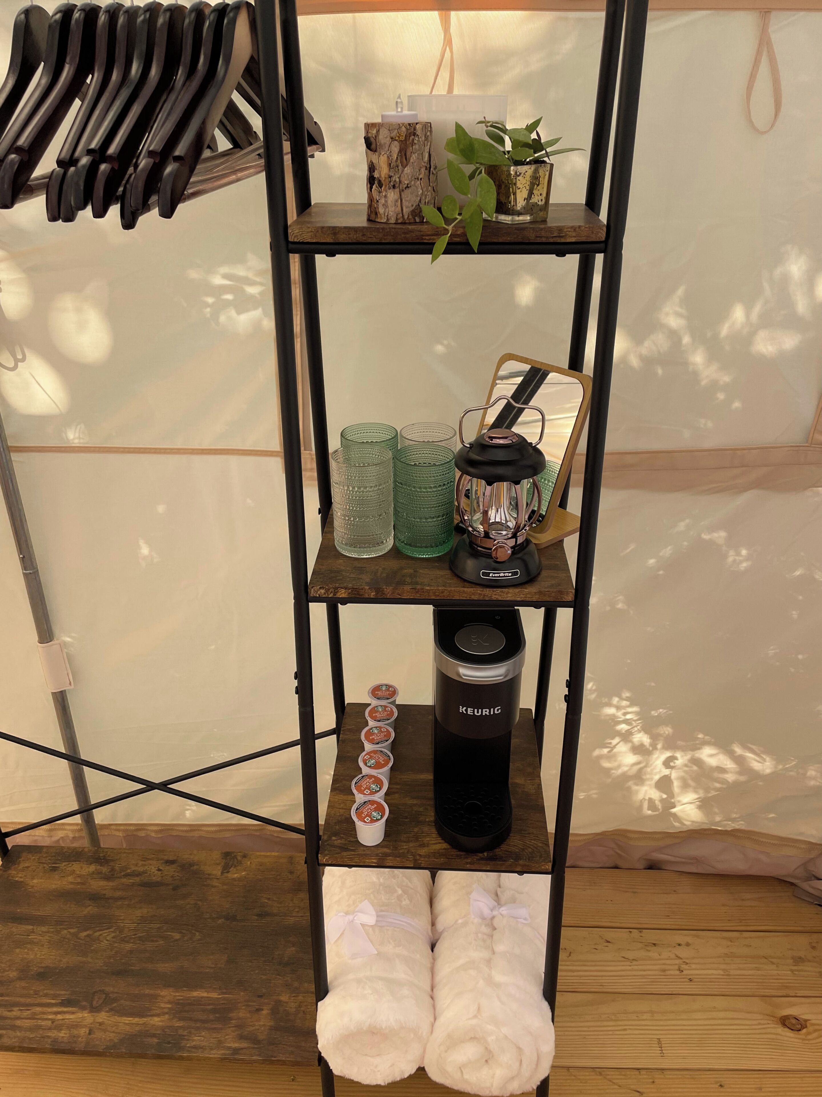 A shelf with a kettle, cups, a lantern, and towels.