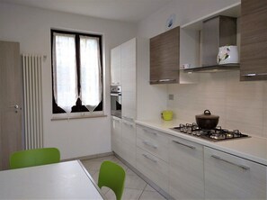 Une cuisine compacte équipée d’une cuisinière à gaz, d’une fenêtre avec des rideaux et d’un coin repas comprenant une table et des chaises.