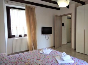 Hotellihuone, jossa on sänky, televisio, ikkuna verhoilla ja vaatekaappi.