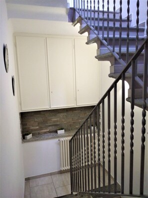 Un escalier avec une balustrade noire menant à un palier doté de meubles blancs et d’une cheminée en pierre.