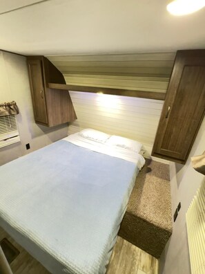 A compact bedroom with a bed, a wooden headboard, and a small window.