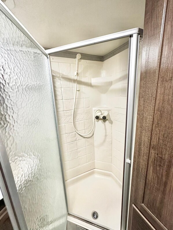 Une douche d’angle avec des carreaux blancs et une porte en verre.