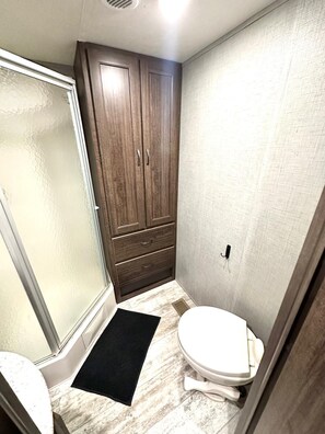 A compact bathroom with a shower, a toilet, and a wooden cabinet.