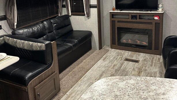 Ein kompaktes Wohnmobil-Interieur mit Ledersofa, Fernseher und integriertem Kamin.