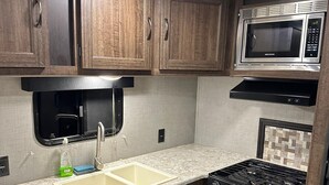 Une cuisine de taille réduite, équipée d’un évier, d’une cuisinière, d’un four à micro-ondes et de meubles de rangement en bois.