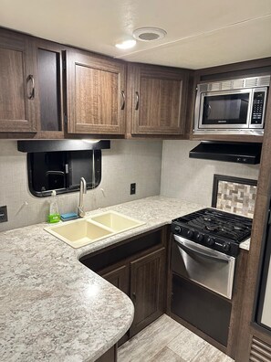 A compact kitchen with a sink, stove, microwave, and wooden cabinets.