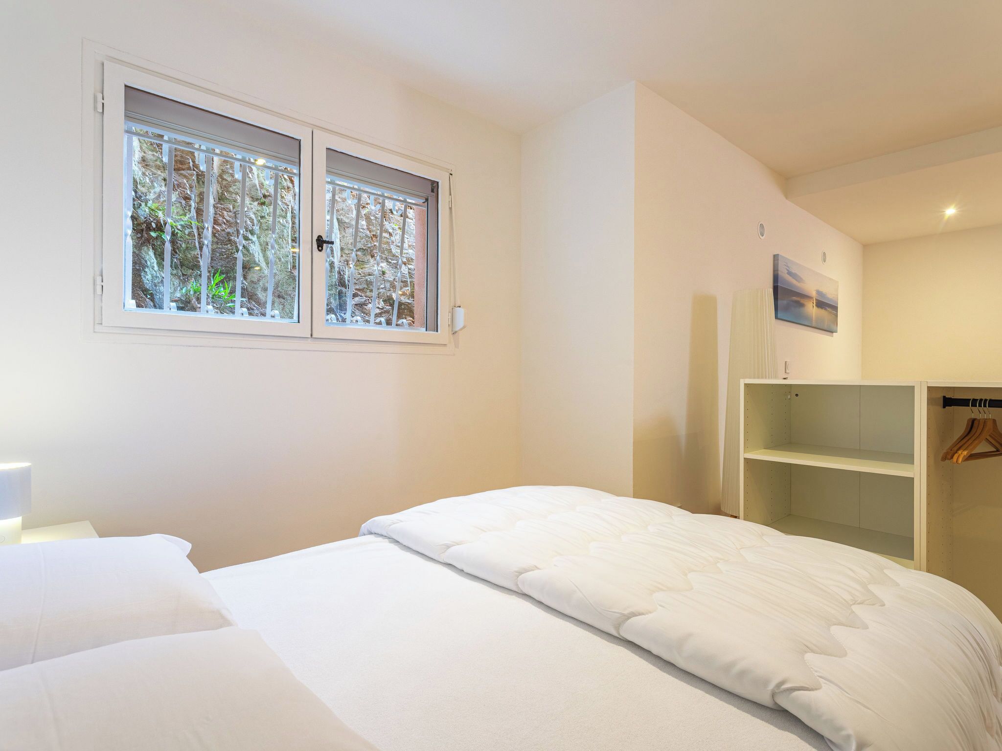 A bedroom with a bed, a wardrobe, a window with a view of trees, and a painting on the wall.