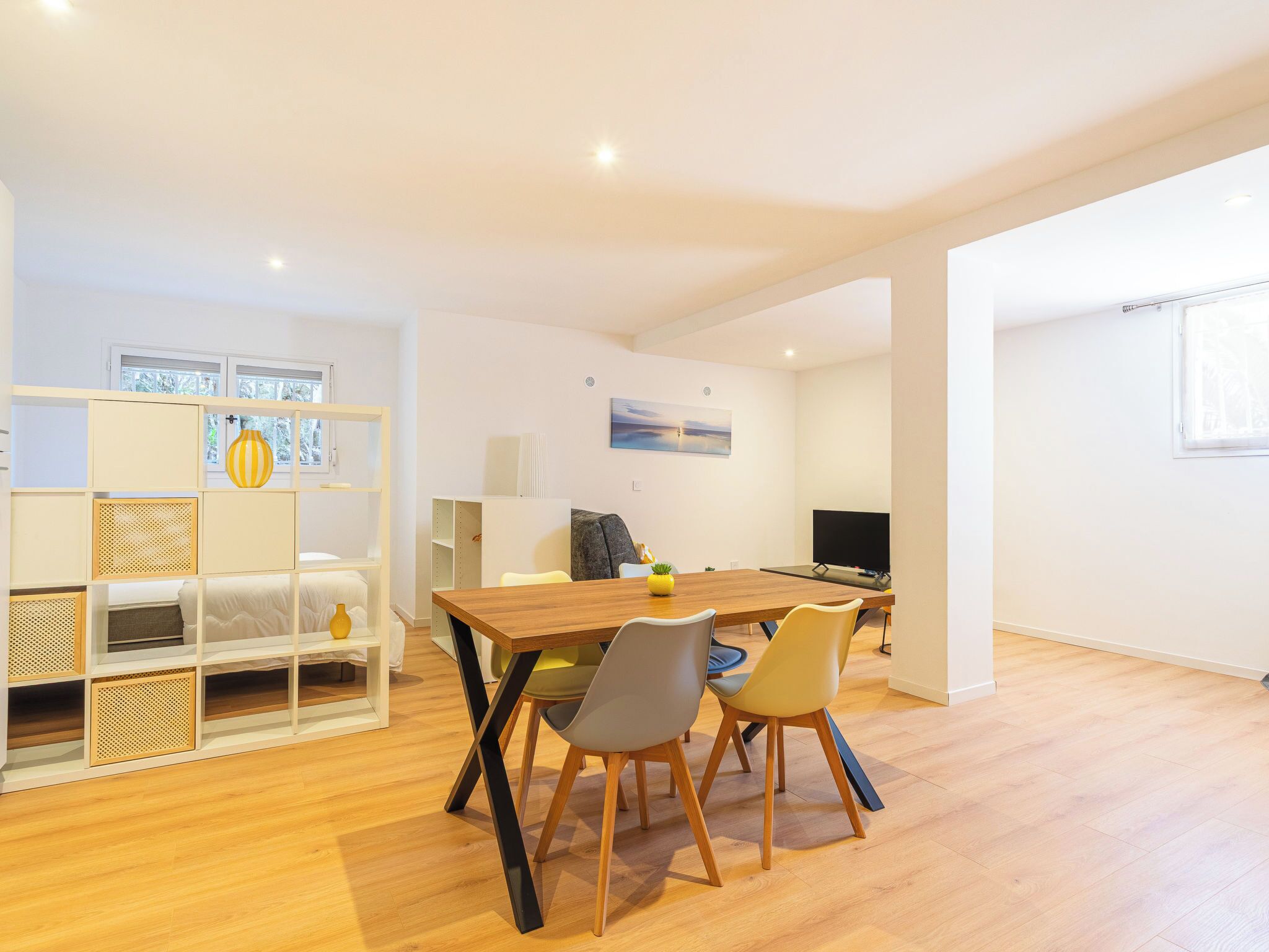A modern living room with a wooden dining table, two chairs, a TV, and a bookshelf.