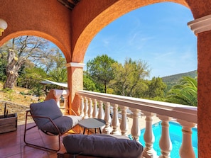 Ein Balkon mit Blick auf Pool und Bäume, ein Stuhl und ein Tisch.