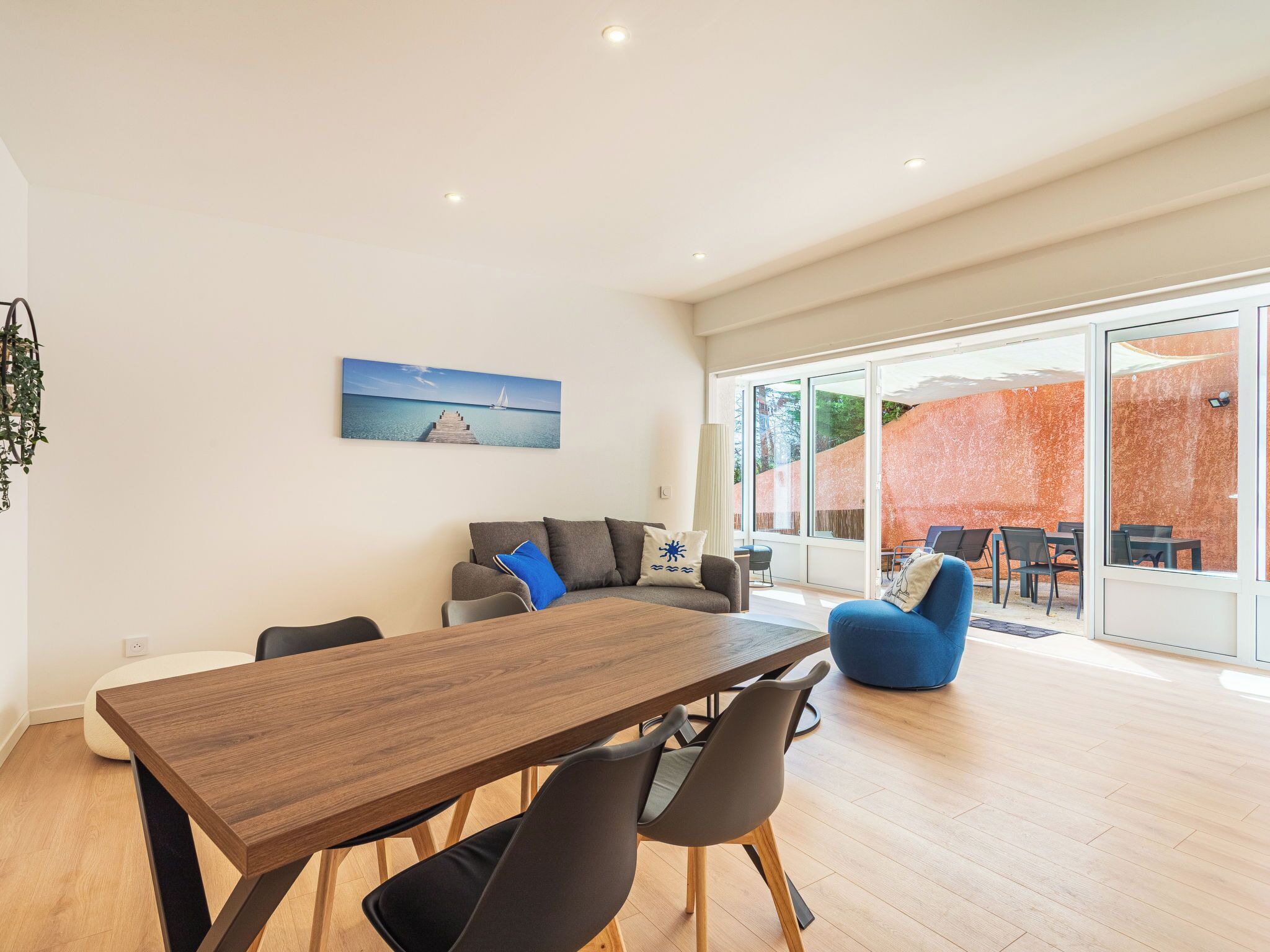 A modern living room with a wooden dining table, grey sofa, and blue armchair.