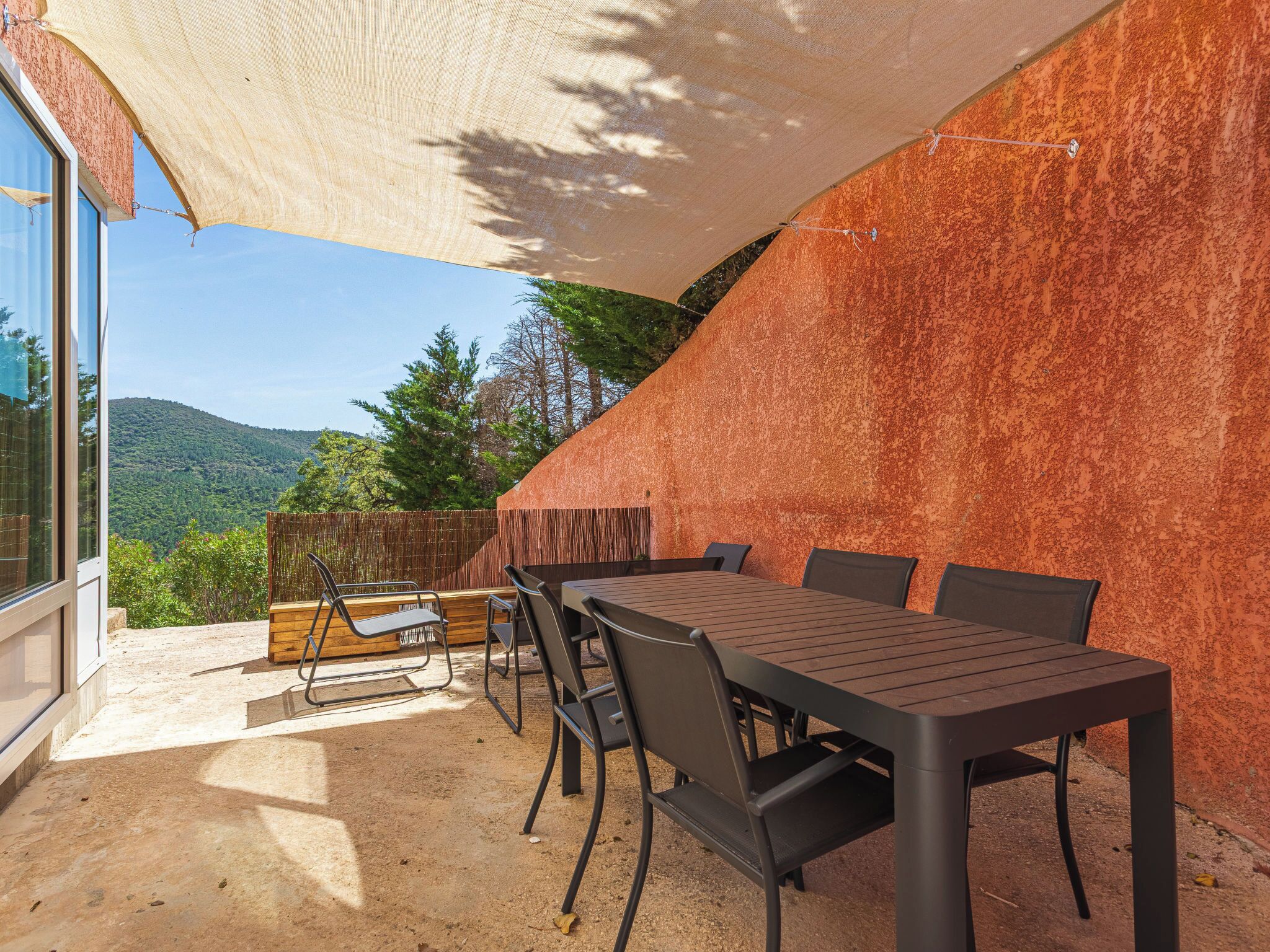 An outdoor patio with a table and chairs, a view of the mountains, and a large shade sail.