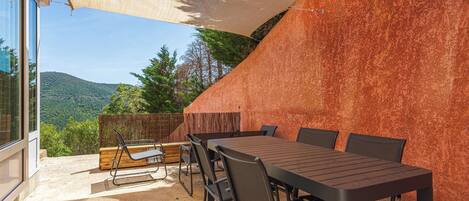 An outdoor patio with a table and chairs, a view of the mountains, and a large shade sail.