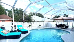 A covered swimming pool with lounge chairs and a table under a transparent roof. - Luxury Pool home, 1 mile from Bush Gardens (Tampa)