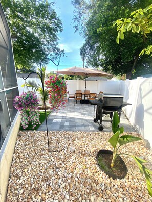 Eine Terrasse mit Tisch, Stühlen, einer hängenden Blumenattrappe und einem Grill.