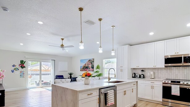 A modern kitchen with white cabinets, a central island, stainless steel appliances, pendant lighting, and a view to the outside. - Luxury Pool home, 1 mile from Bush Gardens (Tampa)