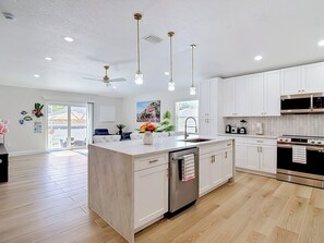 A modern kitchen with white cabinets, a central island, stainless steel appliances, pendant lighting, and a view to the outside. - Luxury Pool home, 1 mile from Bush Gardens (Tampa)