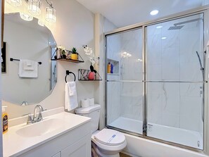 Ein modernes Badezimmer mit Duschkabine aus Glas, einem weißen Waschbecken, einer Toilette und einem Spiegel mit Ablageflächen darüber.