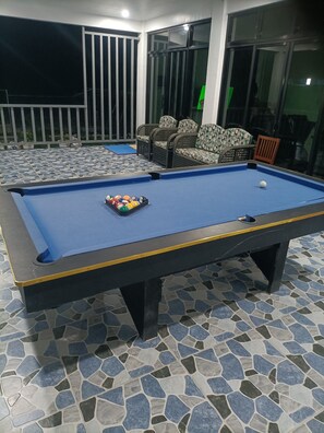 A pool table with a blue felt surface, surrounded by a tiled floor with a mosaic pattern.