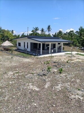 A single-story house with a porch, surrounded by a fenced yard with sparse vegetation.