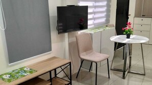 Une chambre moderne avec un téléviseur fixé au mur, une petite table ronde agrémentée d’une plante en pot, un banc et une chaise.