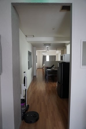 Un couloir mène à une cuisine équipée d’un réfrigérateur, d’une table à manger et d’un ventilateur de plafond.