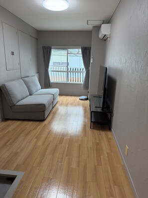 A living room with a grey sofa, a TV stand, a wooden floor, and a window with curtains. - Within walking distance of Shibuya, Harajuku and Shinjuku! 86 sqm spacious family size apartment with balcony (渋谷区)