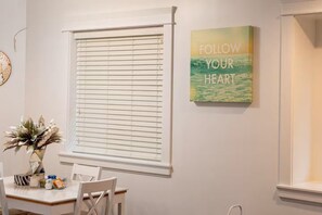 Ein Essbereich mit Tisch, Stühlen, einem Fenster mit Jalousien und einem motivierenden Plakat an der Wand.