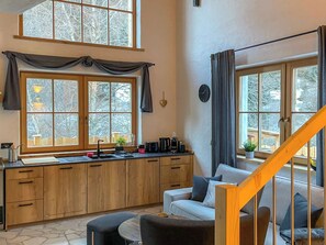 A modern kitchen with wooden cabinets, a built-in sink, and a dining area with a white sofa and ottoman. - Chalet Auszeit by Interhome (Flattach)